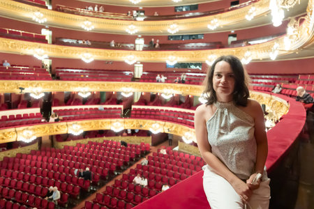 Interested young adult brunette sitting on balcony of classic concert hall