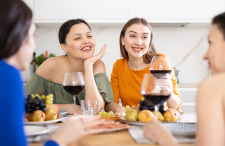 Four women are sitting at table, enjoying food and wine, chatting, talking, laughing.の写真素材
