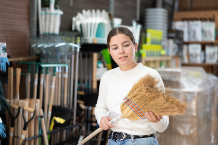Girl carefully chooses broom in hardware store to clean yard of her house