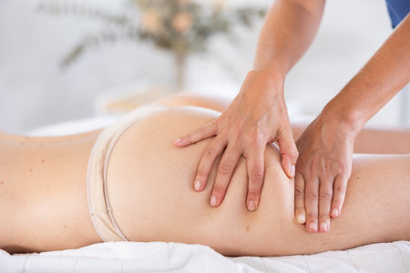 Hands of professional masseuse performing anti-cellulite massage to woman