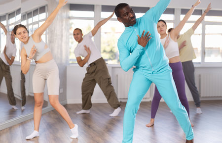African american man and group of young active sports people practicing rock and roll dance in dance hallの写真素材
