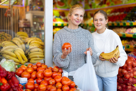 Smiling teenage girl with mother choosing fruits and vegetables in supermarketの写真素材