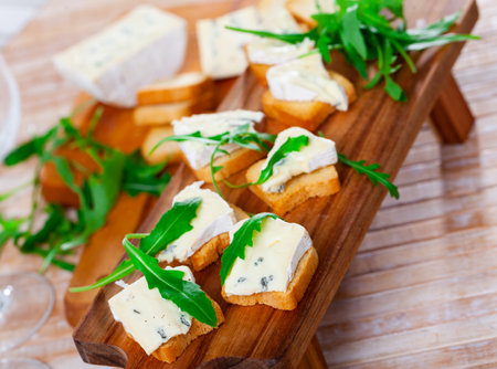 On table there is cutting board with blue cheese and hardtack decorated with arugulaの写真素材