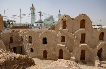 KSAR HADADA, TUNISIA - MARCH 03, 2024: Scenic view of ancient weathered Berber earthen ghorfas contrasting with modern mosque in background under warm Tunisian spring sun in village of Ksar Hadadaのeditorial素材