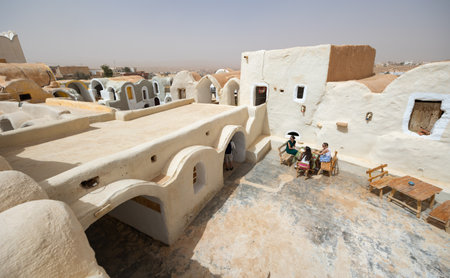 KSAR HEDADA, TUNISIA - MARCH 03, 2024: Tourists relaxing in sunlit courtyard at racy hotel in Tunisian village of Ksar Hedada, surrounded by ancient Berber earthen ghorfas adopted for guest roomsのeditorial素材
