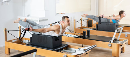 Atletic man doing pilates exercises with reformer bed in studio. Active lifestyle and fitness conceptの写真素材