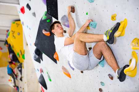 Young man grabbing ledges of artificial climbing wall