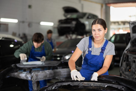 Young female auto mechanic sanding car bumper with sandpaper