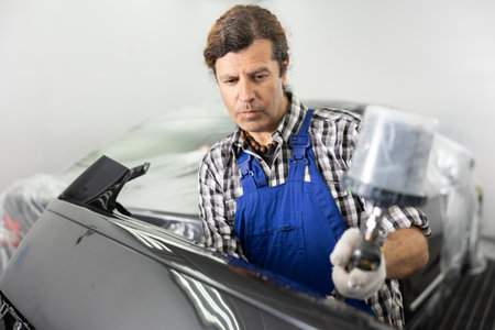 Adult male mechanic paints car with machineの写真素材