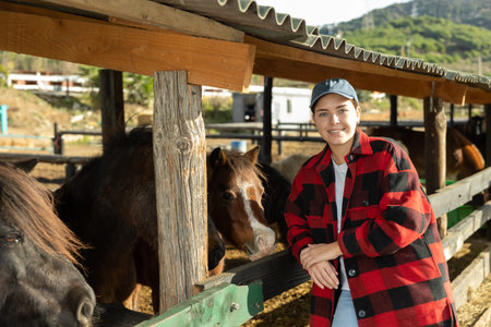 Portrait of smiling woman next to pony in stall at livestock farm