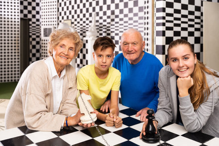 Grandparents with grandchildren are satisfied after visit of escape room stylized under chess board