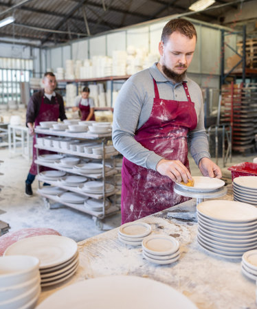 Skilled artisan cleaning plates with sponge in ceramics studio