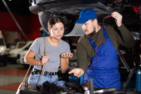 Skilled male auto mechanic measuring capacity of automobile of young girl