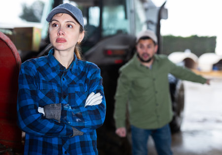 Upset young workwoman standing near tractor in farm backyardの写真素材
