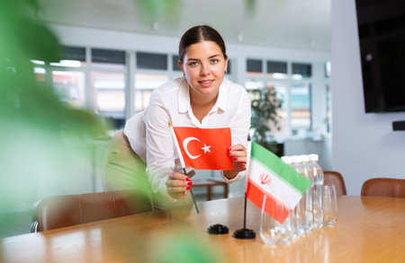 Positive young woman putting little flag of Turkey on table next to the flag of Iranの写真素材