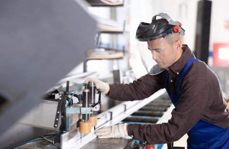 Glass workshop - man works on machine for cutting aluminum profiles for windows