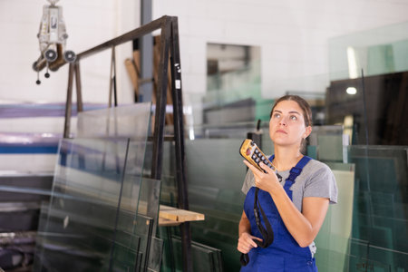 Female worker using remote control to operate machinery in glass workshopの写真素材