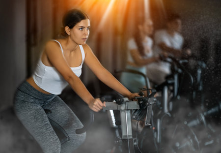 Portrait of a slender girl on a stationary bike in gymの写真素材
