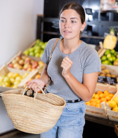 Female shopper with wicker basket in trading floor browses eco product in bio shop search fruit goodの写真素材