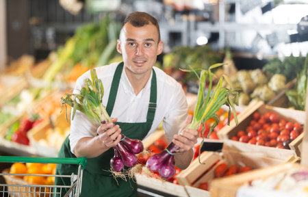 Man supermarket worker with onion in hands examines productの写真素材