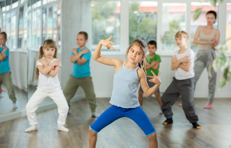 Positive juvenile girl engaged in breakdancing in training room with childrens group