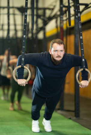 Bearded guy performing push-ups in gymnastic rings at gym