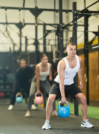 Sportive young man lifting heavy kettlebell in sports hall