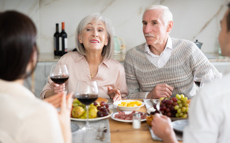Senior parents sitting at table drinking wine and having conversation with young coupleの写真素材