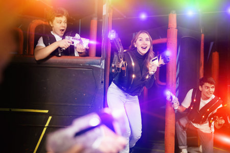 Laughing players mens and womens playing in teams in dark laser tag station