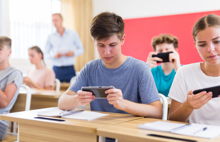 Young students with smartphones sitting in class room