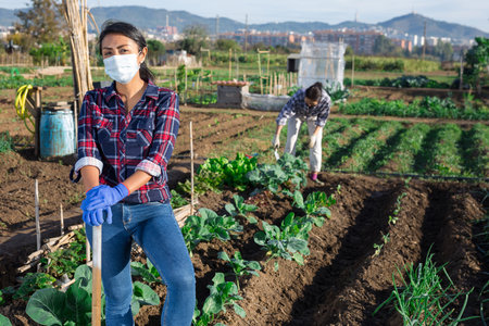 Woman gardener wearing face mask for prevention corona virus and holding shovel in gardenの写真素材