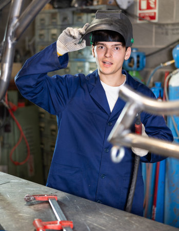 Smiling young male welder standing in metal workshop