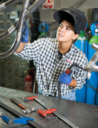 Portrait of a female welder standing with a welding machine and a safety helmet in metal machining...