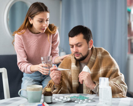 Man with viral disease sitting at home table with worried wifeの写真素材