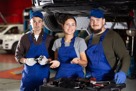 Two positive car mechanics and female worker inviting clients in auto service shopの写真素材