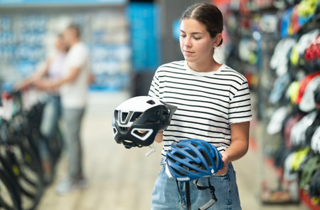 Positive female customer choosing safe bicycle helmet in sports bike store