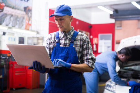 Mechanic man using laptop checking car in workshopの写真素材
