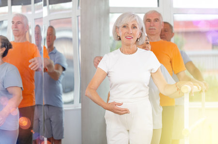 Happy mature woman in sportswear, participating first position of ballet stance at barre with group people standing in row in choreography studioの写真素材