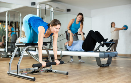 Middle-aged woman practicing pilates on pedal fitness chair in sports hallの写真素材