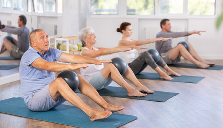 Group of mature people in sportswear exercising Pilates with soft balls while sitting on mats in fitness studioの写真素材