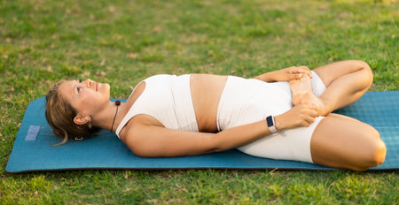 Girl relaxing in Supta Baddha Konasana on mat on green grass