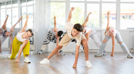 Teen guy together with group of teenage friends, learn to dance hip hop in choreographic hall.