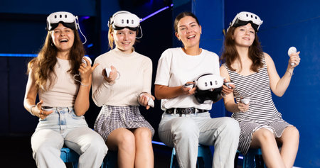 Portrait of happy four girlfriends wearing virtual reality glasses together in dark room