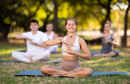 Yoga lesson visitors with girl coach perform padmasana in parkの写真素材