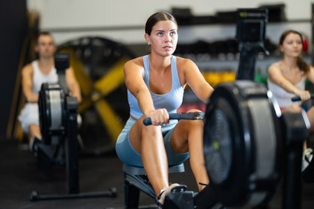 Young woman training at cable row machine with group of sporty people in CrossFit gymの写真素材