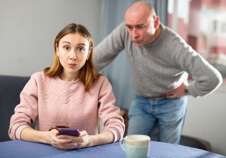 Man controling how woman is texting with someone on a mobile phoneの写真素材