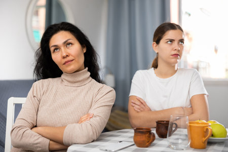 Offended women sitting at table in apartmentの写真素材