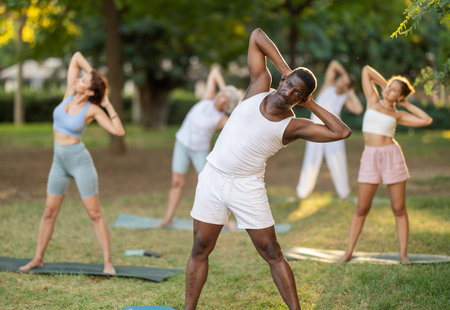 African man doing Tiryaka Tadasana during group yoga in parkの写真素材