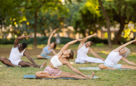 Multinational yoga enthusiasts with female coach perform Janu Shirshasana in parkの写真素材