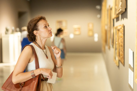 Side view of young intelligent woman looking at exhibition of paintings in museumの写真素材